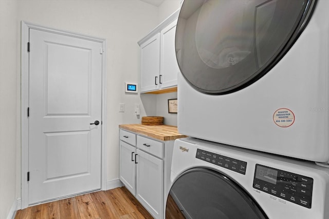 clothes washing area featuring light wood-type flooring, cabinets, and stacked washing maching and dryer