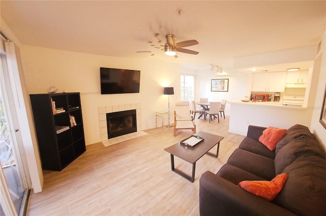 living room with ceiling fan, a tile fireplace, and light hardwood / wood-style flooring