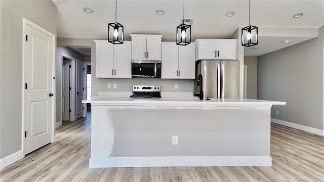 kitchen with hanging light fixtures, appliances with stainless steel finishes, light wood-type flooring, and a kitchen island with sink