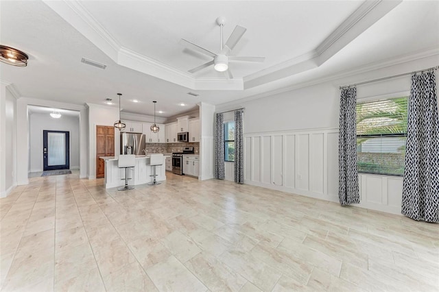 unfurnished living room with ornamental molding, ceiling fan, and a raised ceiling