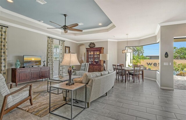 living room with a raised ceiling, crown molding, and ceiling fan