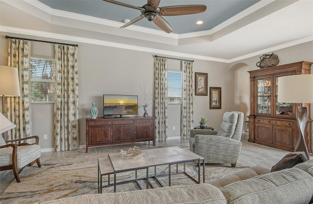 living room featuring a raised ceiling, ornamental molding, a healthy amount of sunlight, and ceiling fan