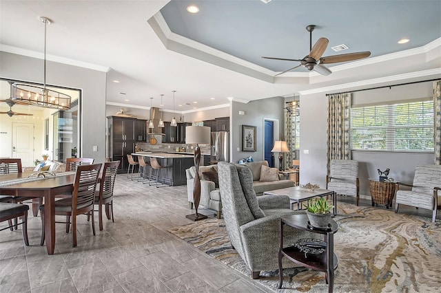 living room featuring a raised ceiling, crown molding, and ceiling fan with notable chandelier