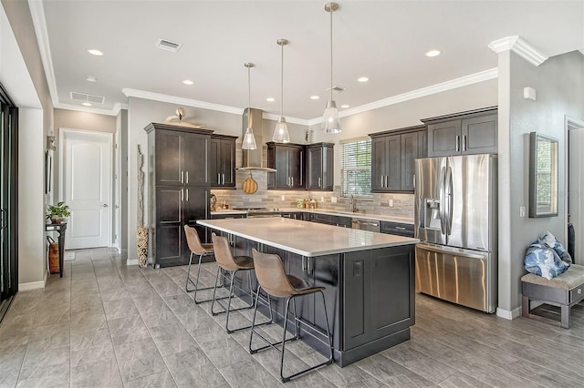 kitchen with hanging light fixtures, stainless steel appliances, a center island, a kitchen bar, and wall chimney exhaust hood