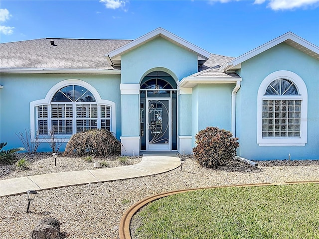 doorway to property with a shingled roof and stucco siding