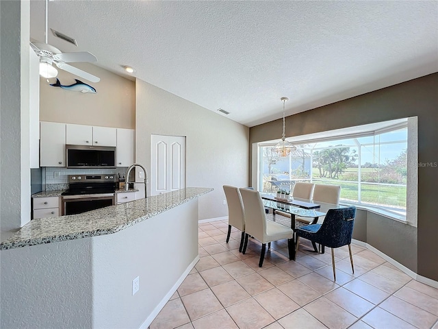 kitchen with appliances with stainless steel finishes, hanging light fixtures, light stone countertops, white cabinets, and lofted ceiling