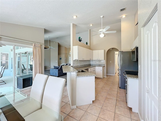 kitchen with ceiling fan, a sink, arched walkways, stainless steel microwave, and vaulted ceiling