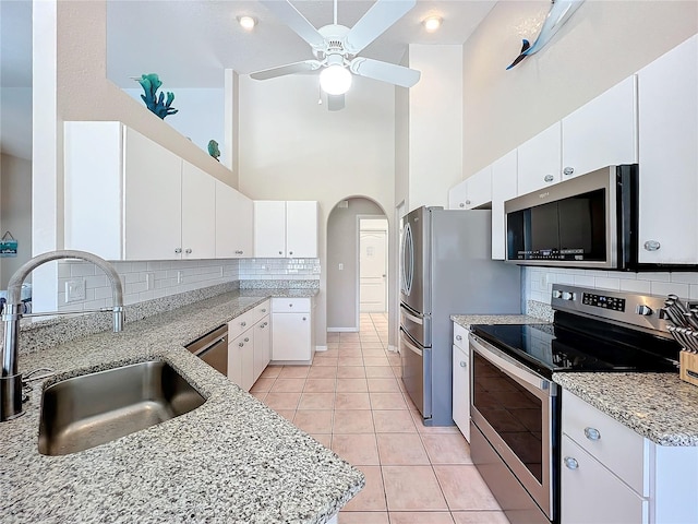 kitchen featuring a high ceiling, sink, white cabinets, light tile patterned floors, and appliances with stainless steel finishes