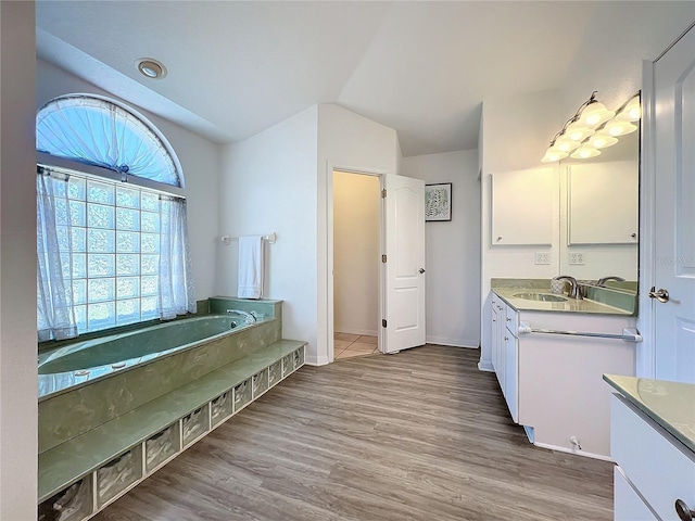 bathroom featuring vanity, baseboards, wood finished floors, vaulted ceiling, and a garden tub