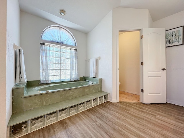 full bath featuring a garden tub, toilet, wood finished floors, and lofted ceiling