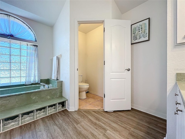 bathroom with lofted ceiling, wood finished floors, toilet, baseboards, and a bath