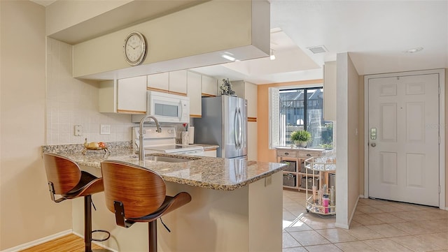 kitchen with white appliances, backsplash, kitchen peninsula, white cabinets, and a breakfast bar area