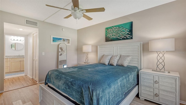 bedroom featuring connected bathroom, light hardwood / wood-style floors, a closet, and ceiling fan