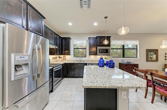 kitchen with sink, light stone counters, appliances with stainless steel finishes, hanging light fixtures, and a center island