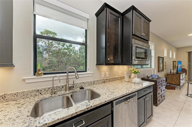 kitchen with stainless steel appliances, sink, light stone countertops, light tile patterned floors, and dark brown cabinets