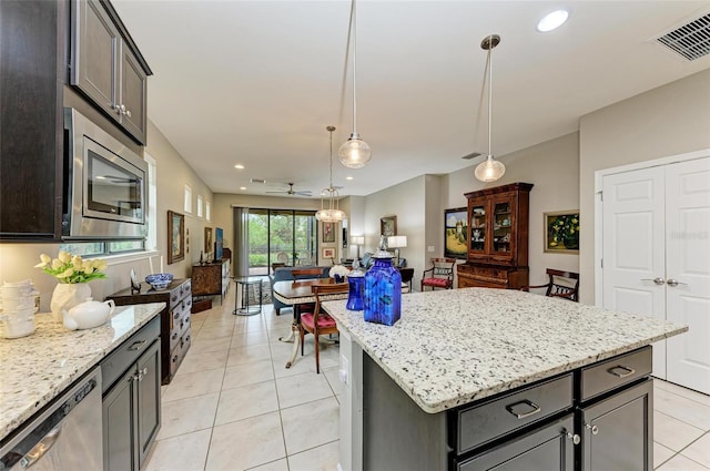 kitchen featuring stainless steel appliances, light stone countertops, light tile patterned floors, decorative light fixtures, and a center island