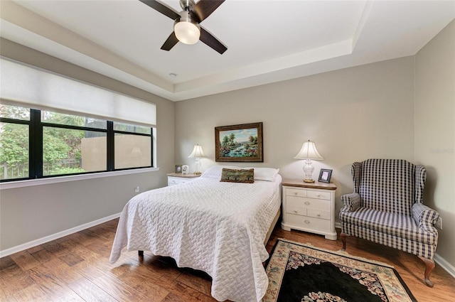 bedroom with hardwood / wood-style flooring, ceiling fan, and a raised ceiling