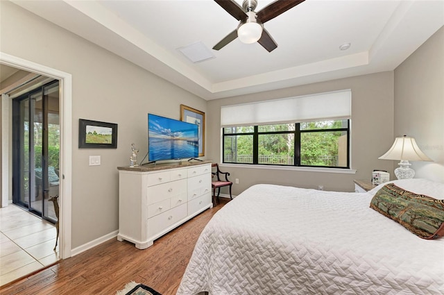 bedroom featuring light hardwood / wood-style floors, ceiling fan, a raised ceiling, and access to outside