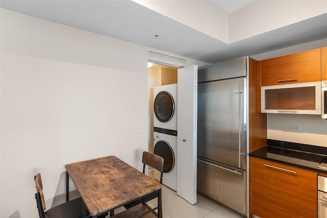 kitchen with stacked washing maching and dryer, light tile patterned flooring, dark stone counters, and built in refrigerator