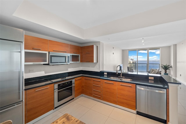 kitchen with kitchen peninsula, light tile patterned floors, appliances with stainless steel finishes, dark stone counters, and sink