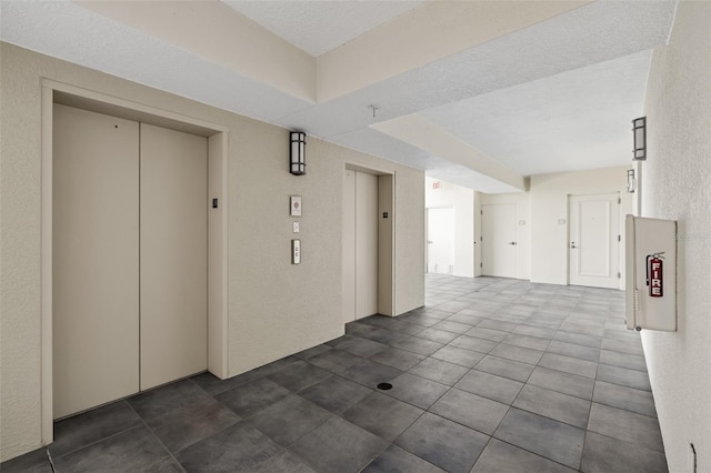 hallway with a textured ceiling, elevator, and dark tile patterned floors