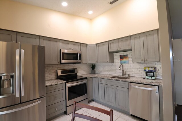 kitchen featuring light tile patterned floors, appliances with stainless steel finishes, light stone countertops, gray cabinetry, and sink