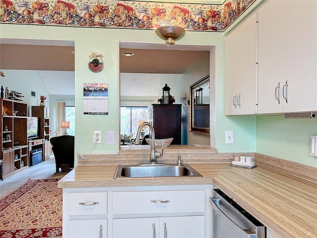 kitchen with sink, carpet floors, lofted ceiling, stainless steel dishwasher, and white cabinets