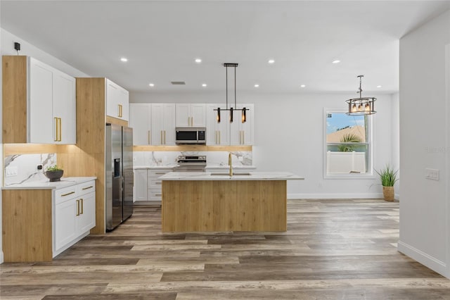 kitchen featuring an island with sink, stainless steel appliances, decorative light fixtures, white cabinets, and light hardwood / wood-style flooring