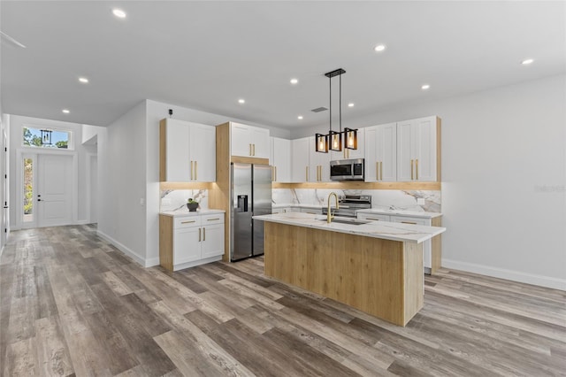 kitchen with a center island with sink, appliances with stainless steel finishes, hanging light fixtures, and light hardwood / wood-style flooring