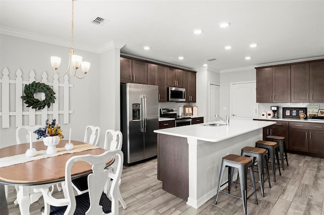 kitchen with backsplash, appliances with stainless steel finishes, light hardwood / wood-style flooring, and an island with sink