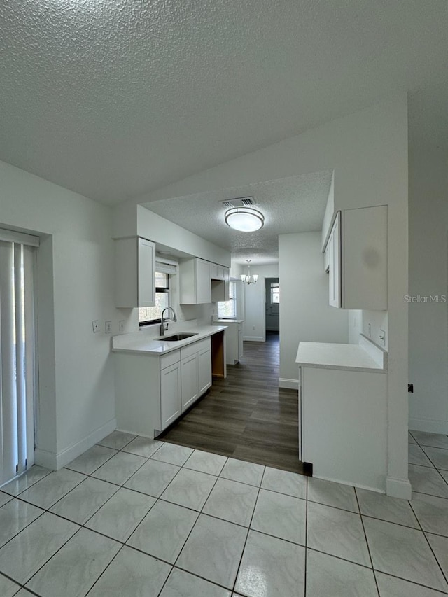 kitchen featuring a notable chandelier, a textured ceiling, sink, white cabinetry, and light wood-type flooring