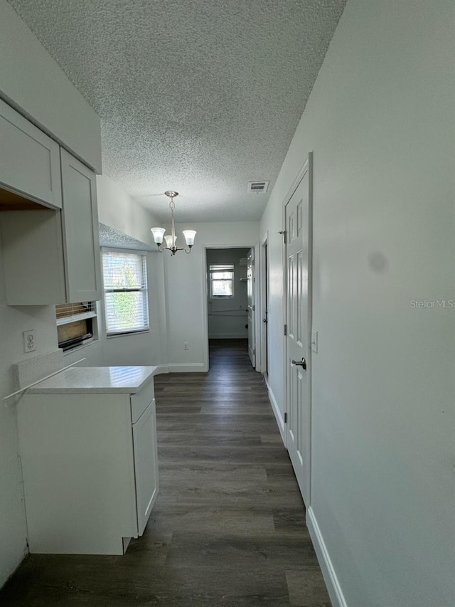 kitchen featuring dark wood-type flooring, a notable chandelier, a textured ceiling, white cabinetry, and decorative light fixtures