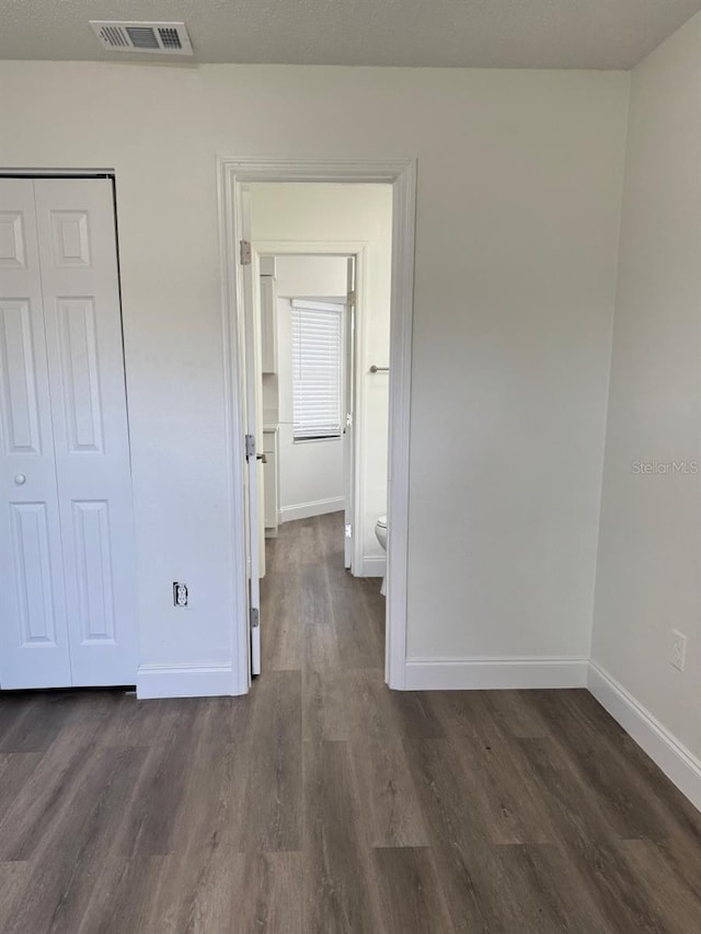 unfurnished bedroom featuring dark wood-type flooring, ensuite bathroom, and a closet