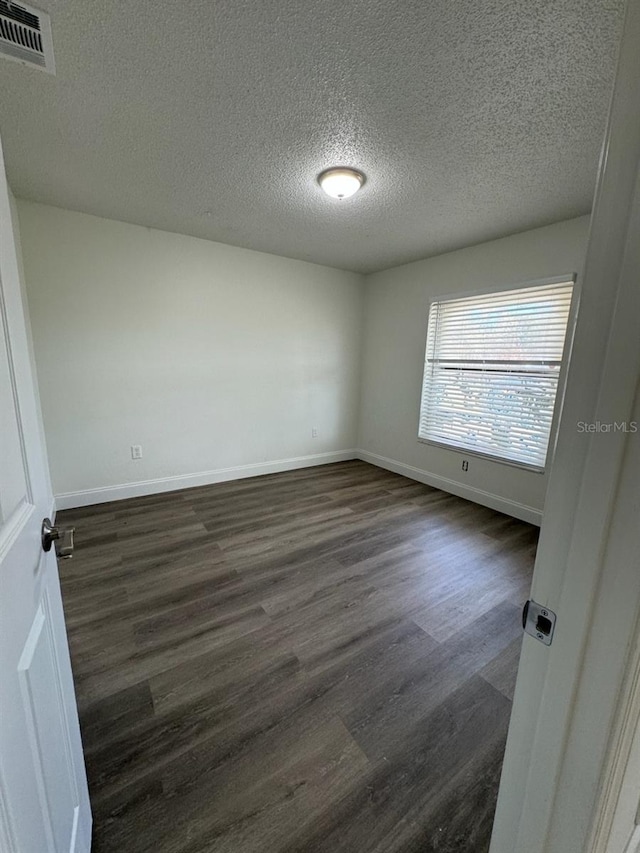 spare room with a textured ceiling and dark hardwood / wood-style flooring