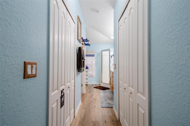 hall featuring vaulted ceiling, a textured ceiling, and light wood-type flooring