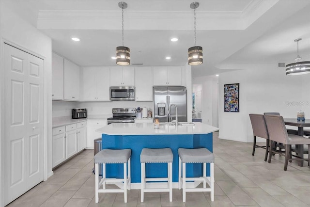 kitchen featuring white cabinets, hanging light fixtures, an island with sink, appliances with stainless steel finishes, and a breakfast bar