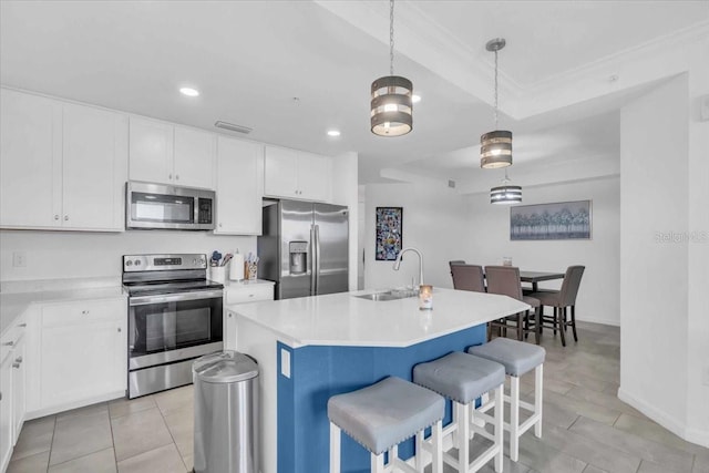 kitchen with white cabinetry, appliances with stainless steel finishes, decorative light fixtures, and a center island with sink