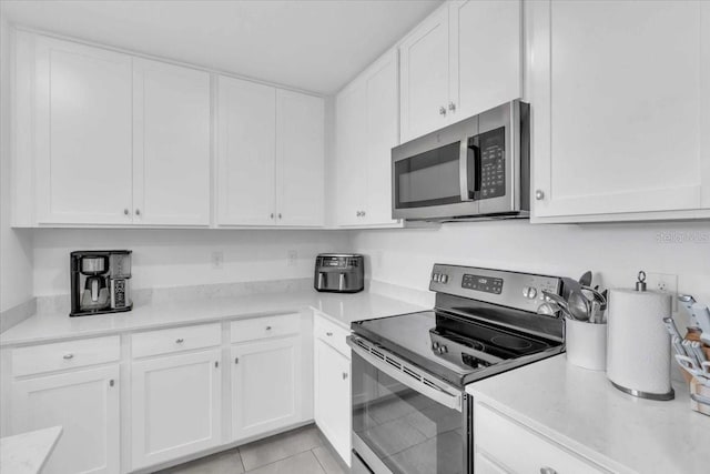 kitchen featuring appliances with stainless steel finishes, light tile patterned flooring, and white cabinets