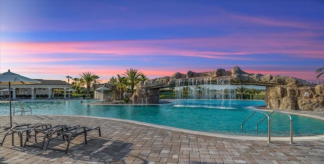 pool at dusk featuring a patio and pool water feature