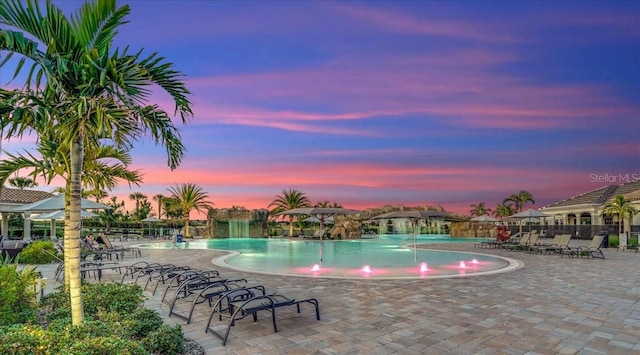 pool at dusk featuring a patio and pool water feature