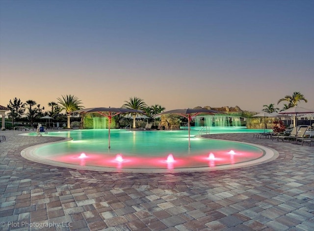 pool at dusk featuring pool water feature and a patio