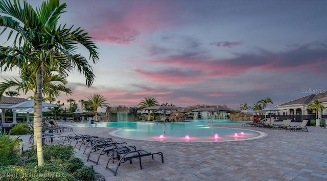 pool at dusk featuring pool water feature and a patio