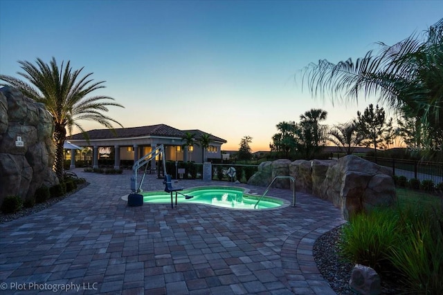 pool at dusk with an in ground hot tub and a patio area