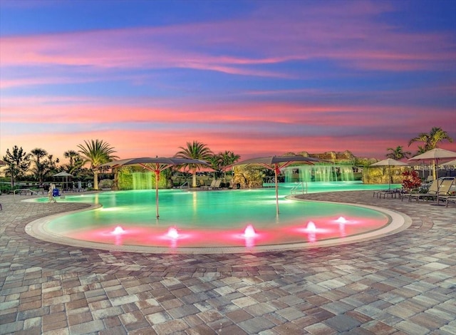 pool at dusk with a patio and pool water feature