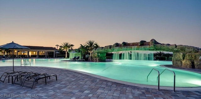 pool at dusk with pool water feature and a patio area