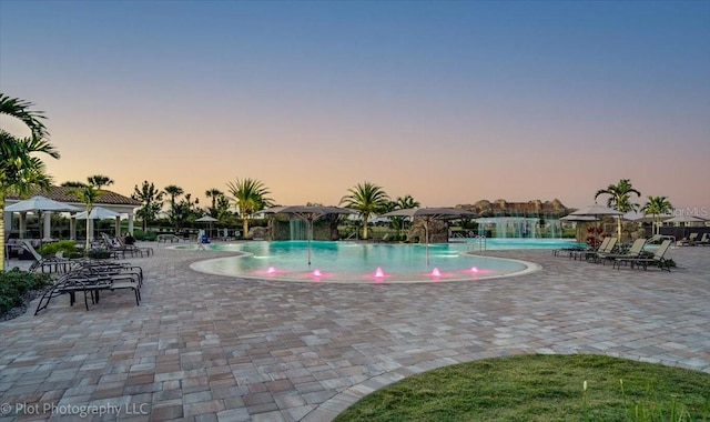 pool at dusk with a patio area and pool water feature