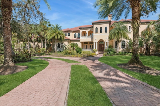 mediterranean / spanish house with a tiled roof, a balcony, a front lawn, and stucco siding