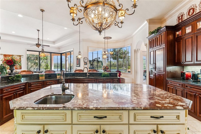 kitchen with arched walkways, a center island with sink, cream cabinets, a sink, and a chandelier