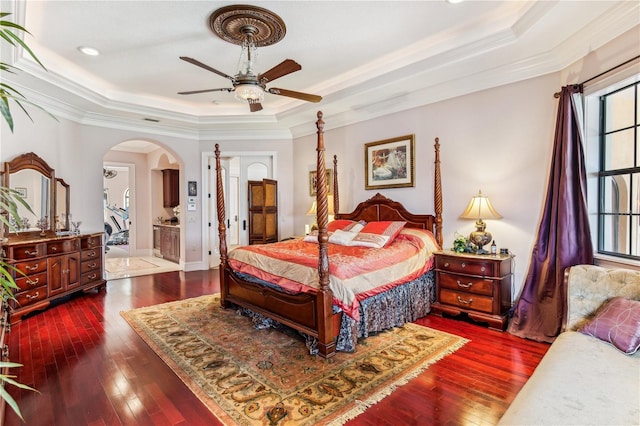 bedroom featuring arched walkways, a tray ceiling, dark wood finished floors, and crown molding