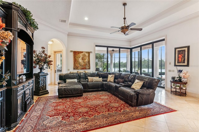 living room featuring a tray ceiling, arched walkways, crown molding, light tile patterned floors, and a ceiling fan